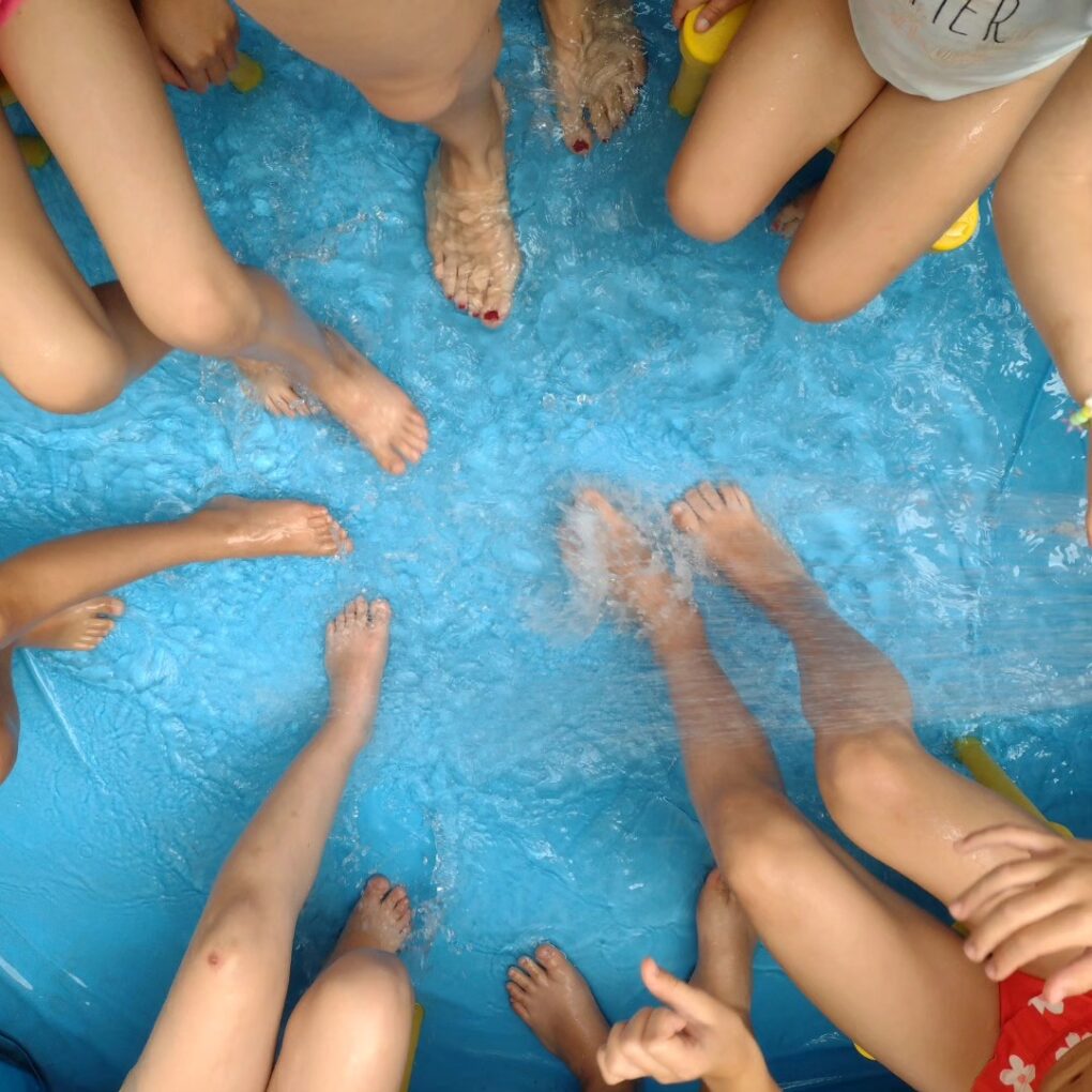 Manos y pies de varios niños dentro de una piscina hinchable en el patio