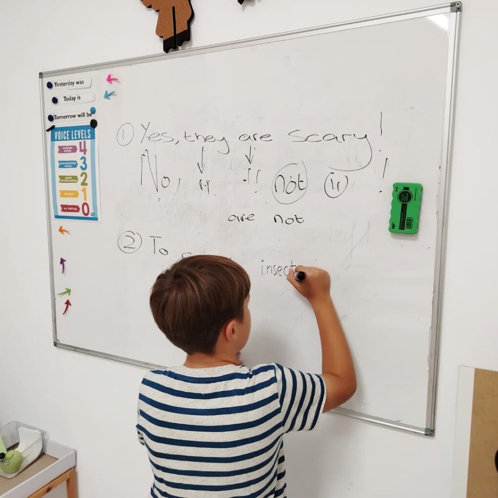 Niño escribiendo una frase en inglés en la pizarra del aula