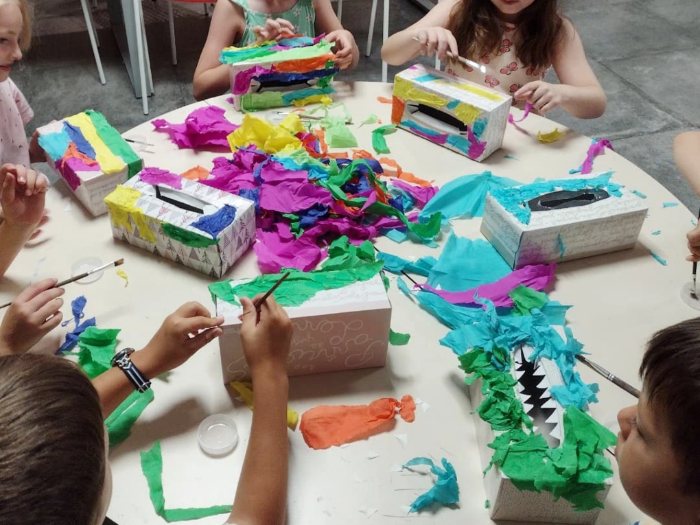 Niños haciendo manualidades con papel de colores alrededor de una mesa