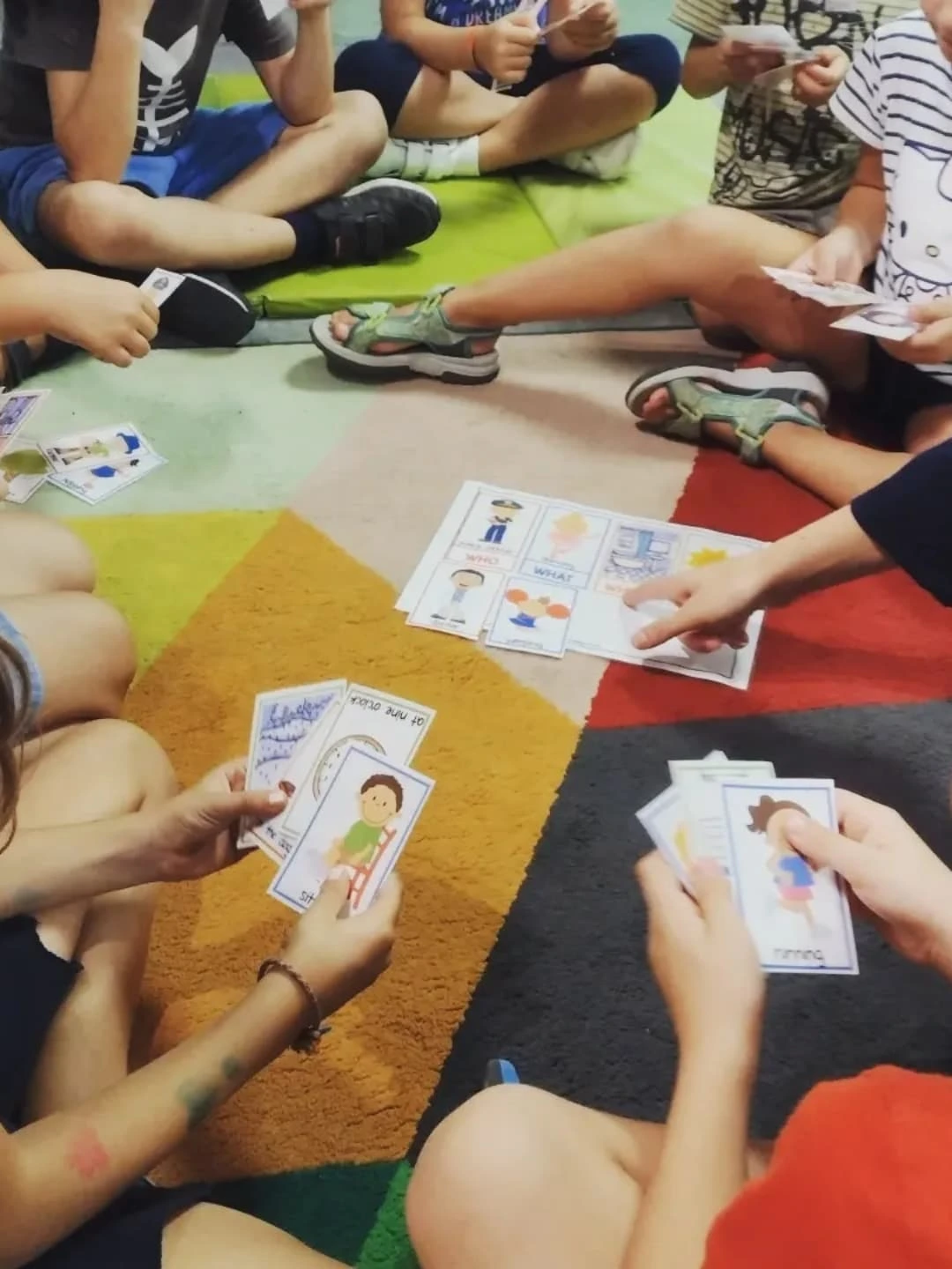 Niños sentados en círculo sobre la alfombra con tarjetas de vocabulario en inglés