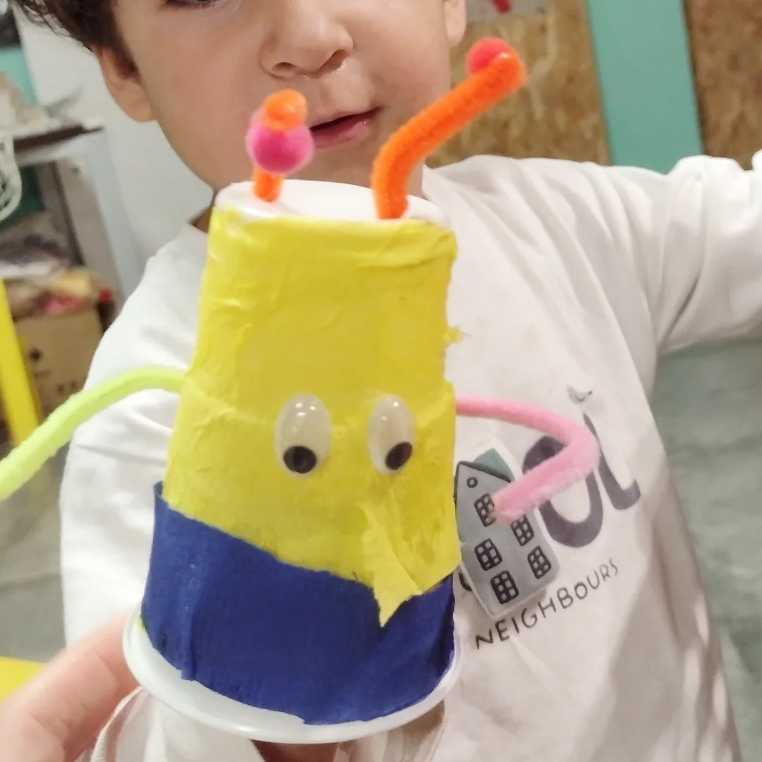 Niña mostrando un personaje hecho con un vaso reciclado en el taller de manualidades